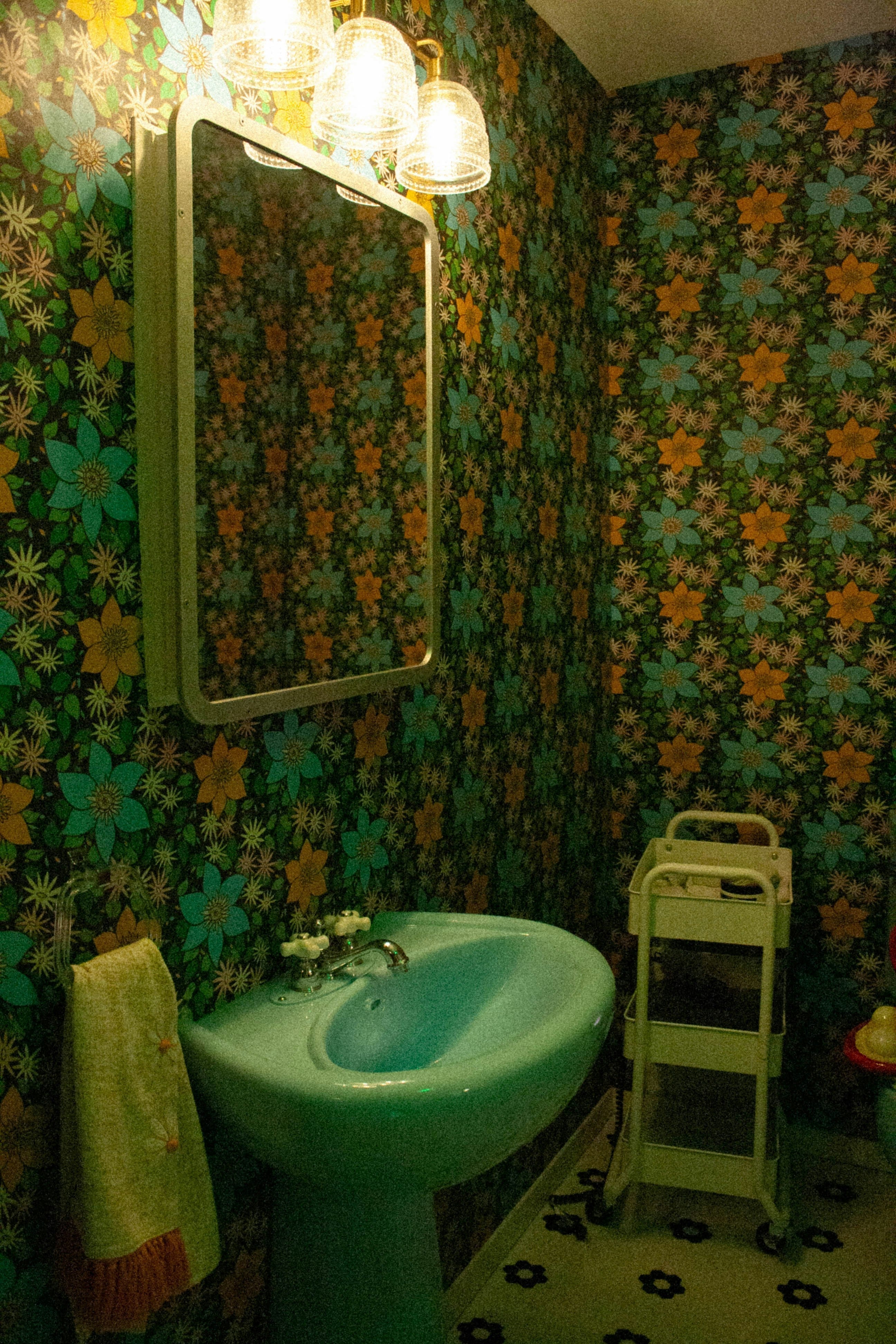 Retro-Badezimmer mit floral gemusterter Tapete, türkisfarbenem Waschbecken und warmem Licht – typisches Badezimmer mit wenig Tageslicht für schattenverträgliche Zimmerpflanzen